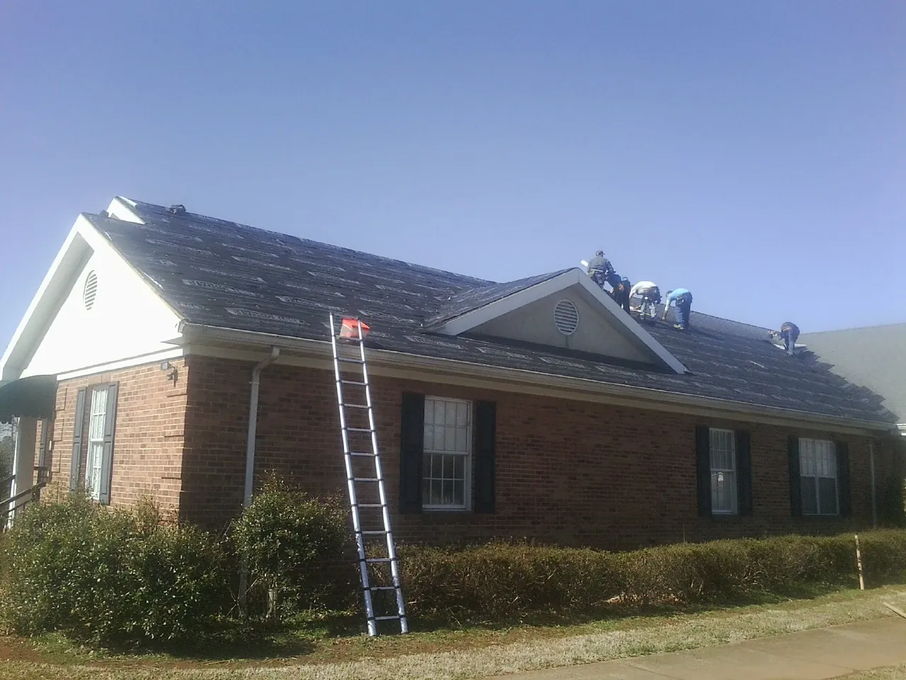 Crew tearing shingles off a brick ranch roof with a ladder set — Metal Roof Repair work by our crew in Port Norris