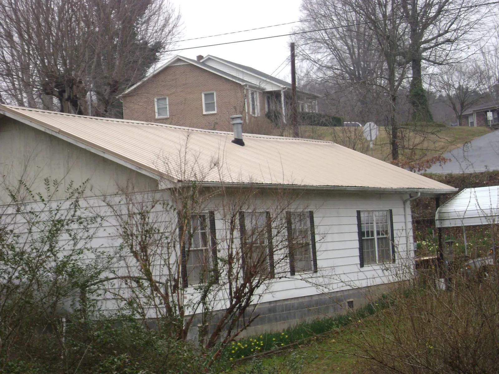 Tan metal roof on a white sided house set into a hillside — Commercial Roofing by Roofing Brothers in Port Norris